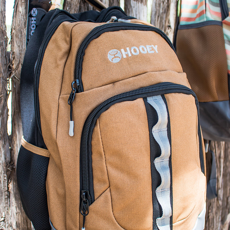 OX tan  backpack with black and grey strap features propped on a fence post