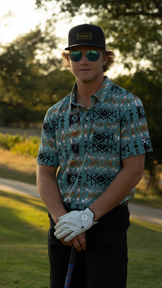 male model posing in teal aztec polo and black shorts on the golf course