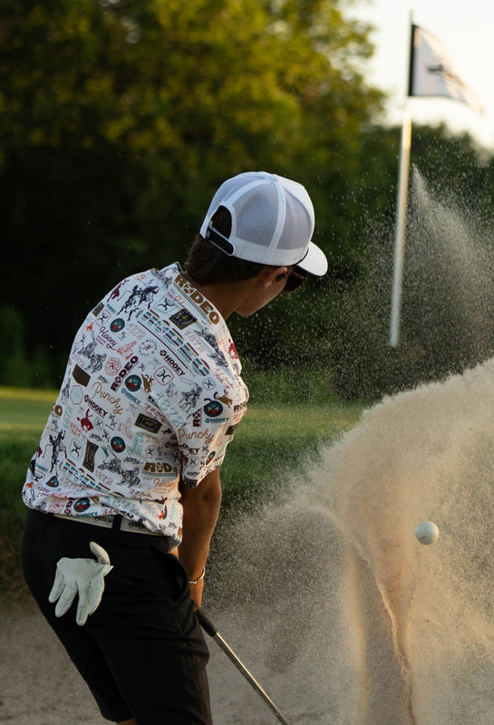 action short of Hooey model hitting a golf ball in the sand, dressed in hooey golf gear