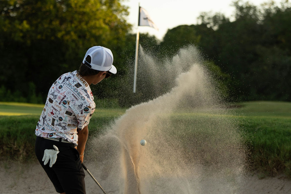 male model dressed in Hooey golf gear, hitting a golf ball out of the sand