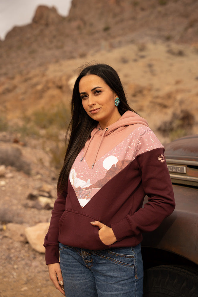 lifestyle image of model wearing a Berkley pink and maroon chevron pattern hoody with desert artwork