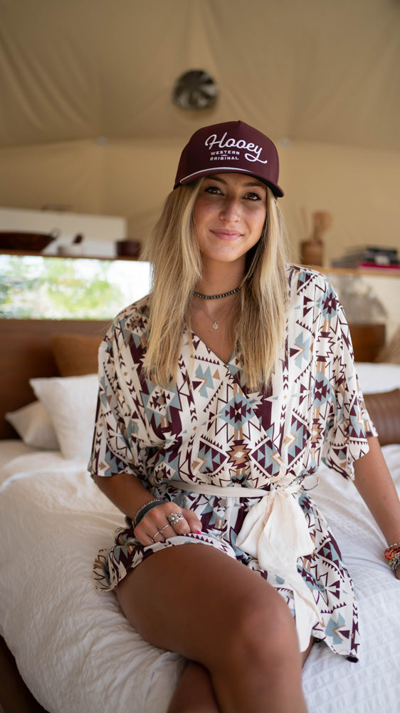 female model posing in a white with Aztec pattern Hooey dress with the maroon and white Hooey OG hat