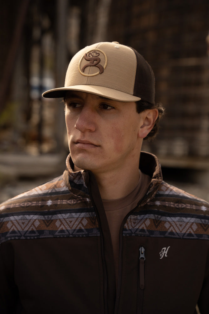 Male wearing brown tech pull over with navy brown and gray Aztec pattern on collar and shoulders with brown and tan Hooey roughy hat