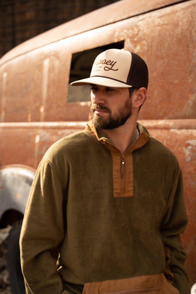 Male model wearing olive and tan fleece pull over with tan and brown Hooey hat