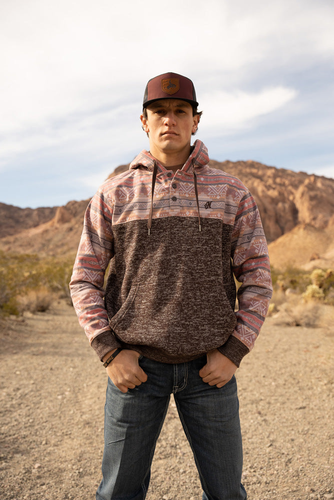 male model wearing the Jimmy heathered grey hoody with purple quilt pattern on sleeves, hood, and collar, roughy hat and jeans in desert setting