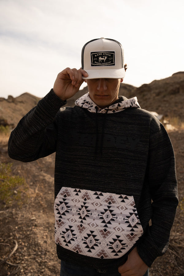 male model wearing the Locl-up heather black hoody with cream, tan, black aztec pattern on pocket and hood in outdoor setting with rank stock hat