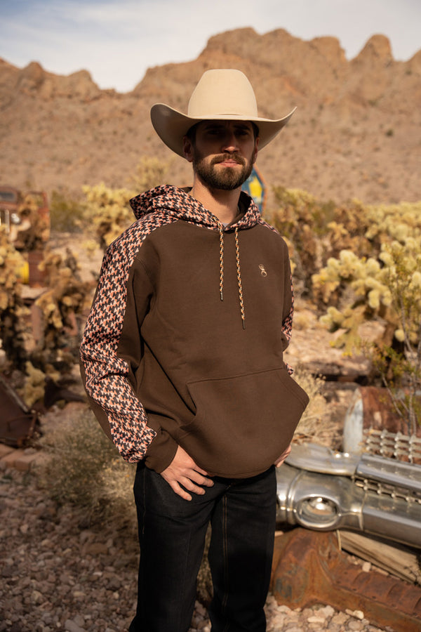 male model sporting the roughy summit brown hoody with cream felt cowboy hat, dark jeans in out door setting 
