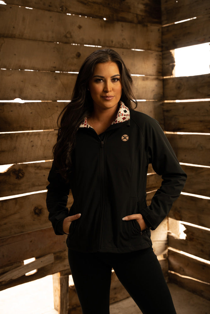 female model wearing black pants and black Hooey pullover posed inside a wooden structure