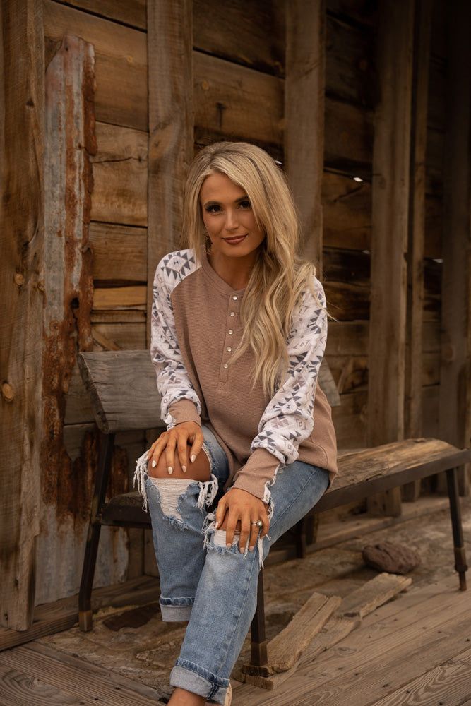 female model wearing ripped jeans, tan and white Henley, posed on rustic wooden bench