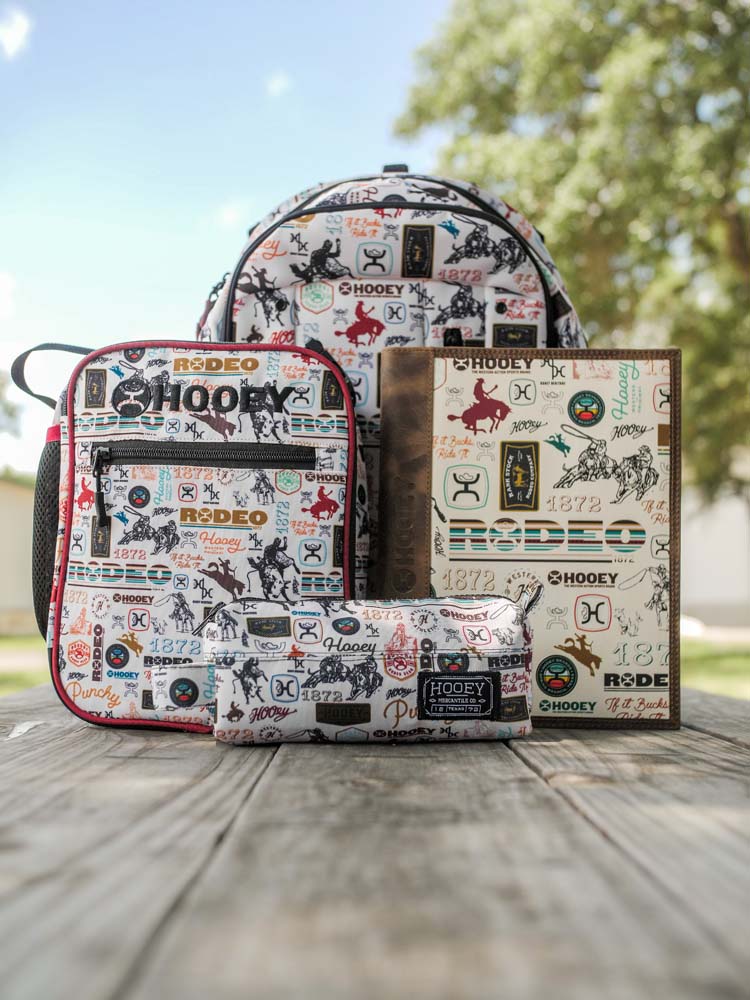 Rockstar, Rodeo pattern collection, lifestyle photo featuring the matching backpack, lunch box, notebook, and travel pouch. All positioned on a picnic table outdoors