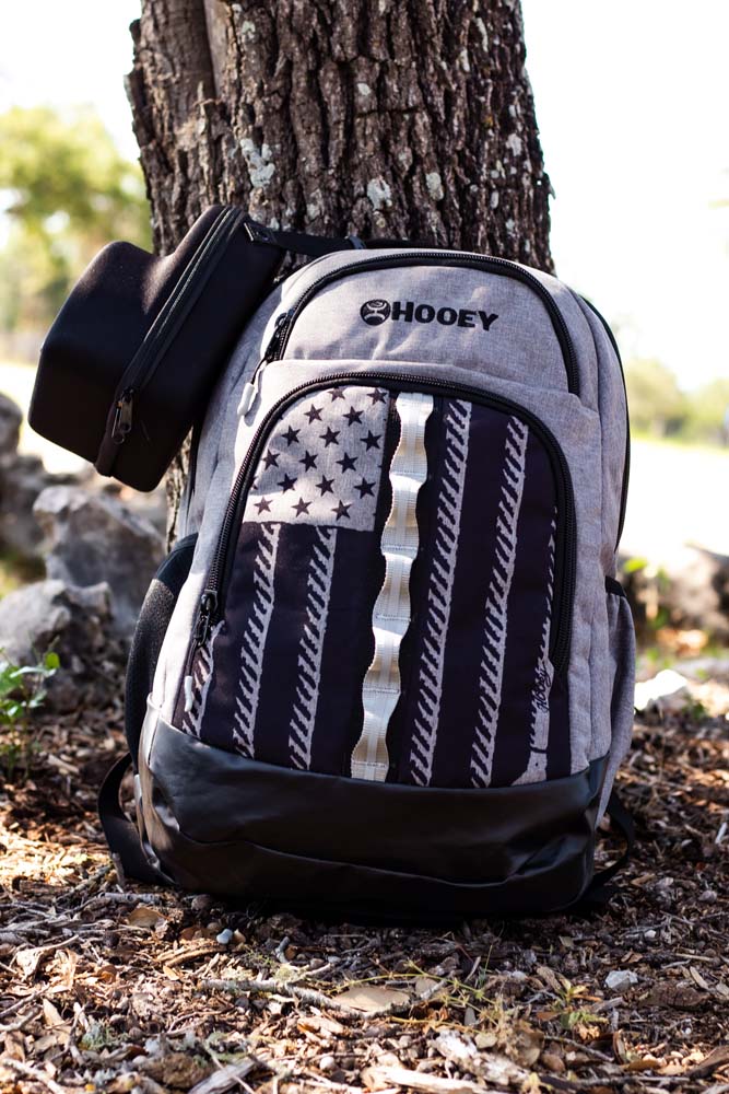 Photo of the Ox grey and black flag backpack propped against a tree trunk with the black cap carrier