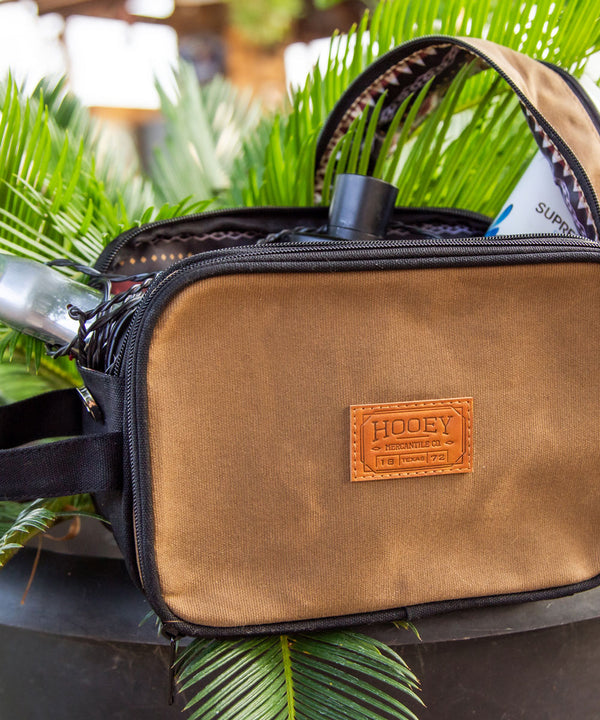 brown and black leather pouch propped on a green leafy plant
