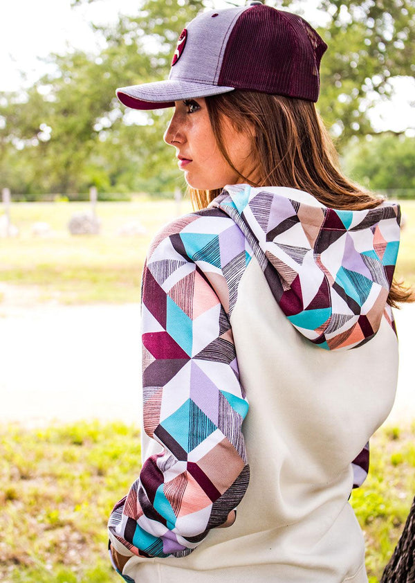 female model sporting the Morocco white hoody with tan, orange, blue, grey, purple patten on sleeves, pocket, and hood with grey and maroon hooey hat in outdoor setting