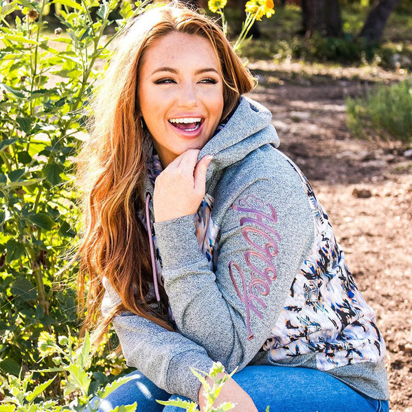 female model sporting hte Maya tan and black aztec pattern hoody with grey sleeves, hood, and cuffs and jeans in outdoor setting