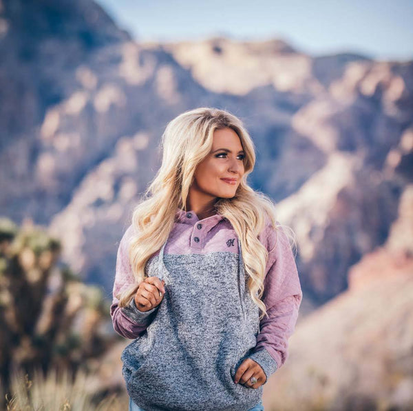 blonde, female model sporting the Jimmy heathered grey hoody with purple quilt pattern on sleeves, hood, and collar in mountainous setting