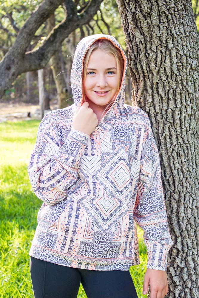 lifestyle image of a young model sporting the Youth Roomy pink and black multi pattern hoody in an outdoor setting