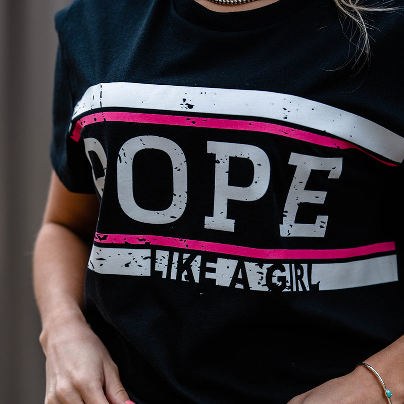 close up of the ROPE like a girl black tee with pink and white stripe logo across the chest being worn by a female model