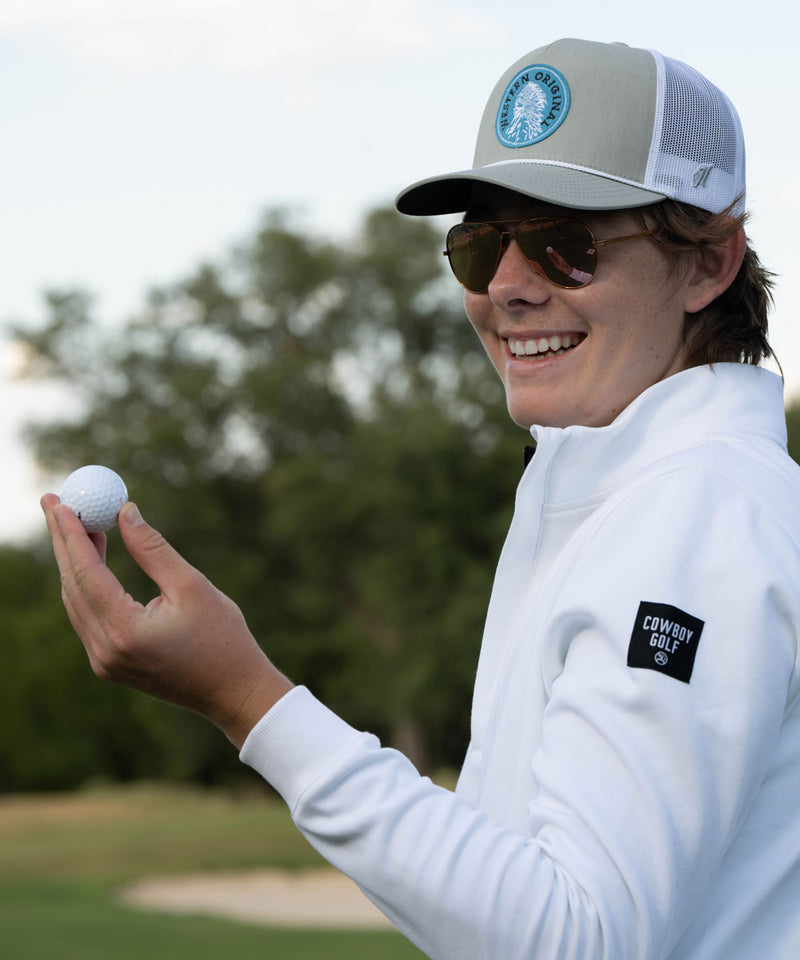 male model wearing white and black golf pullover with tan and white hat holding golf ball