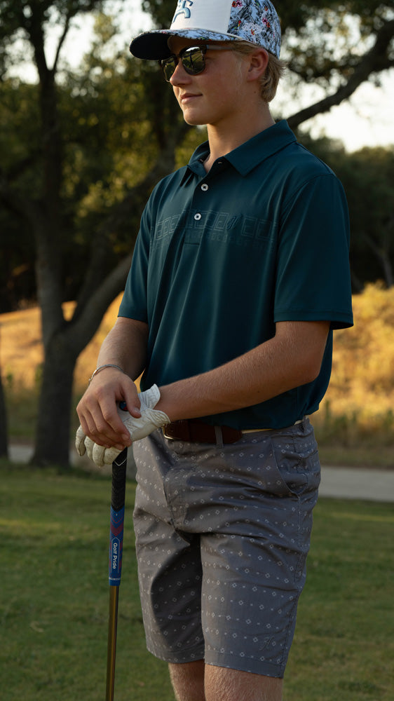 male model posing in green golf polo and grey shorts on the golf course