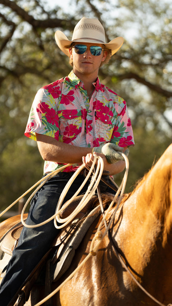 male model wearing Hooey's Hawaiian pattern sol shirt, jeans, and cowboy hat white riding horse back and holding rope