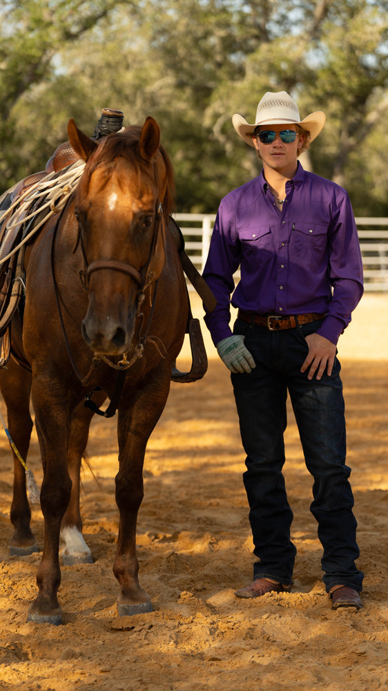 male model standing with horse while wearing Hooey's dark wash jeans and purple sol shirt