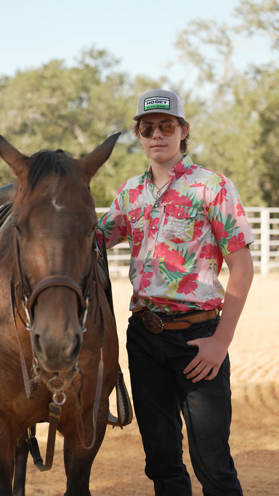 male model wearing Hooey hat, Hawaiian print button down and dark wash jeans while posing with a horse