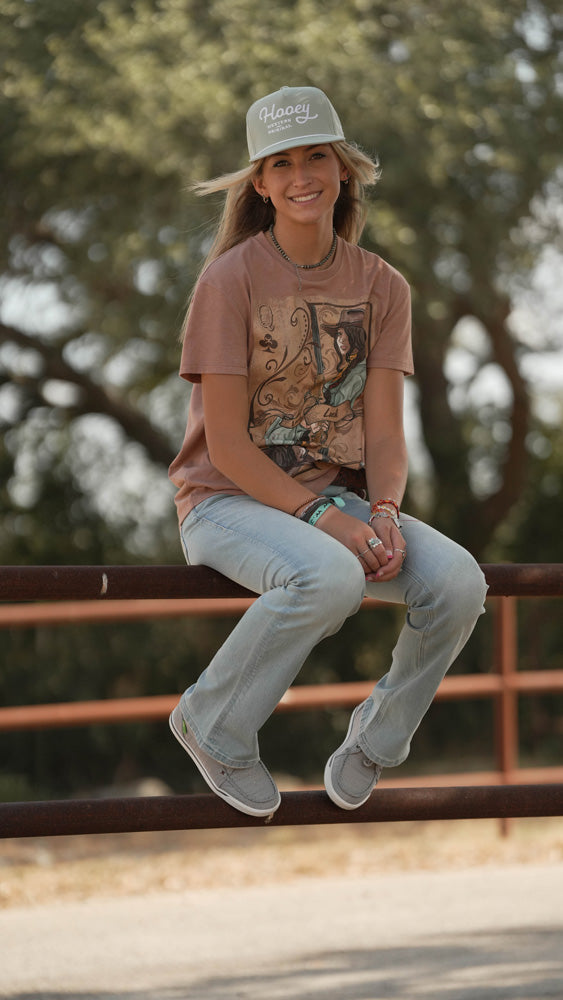 female model posing in grey hat, peach tee, and light wash jeans