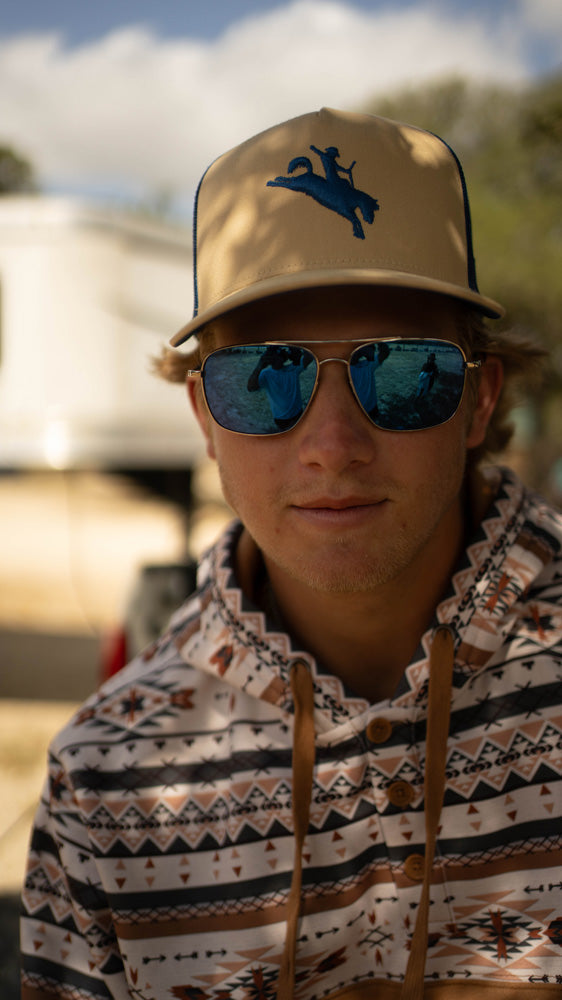 close up of male model wearing tan and black hat with white/grey/brown Aztec pattern hoody in outdoor setting