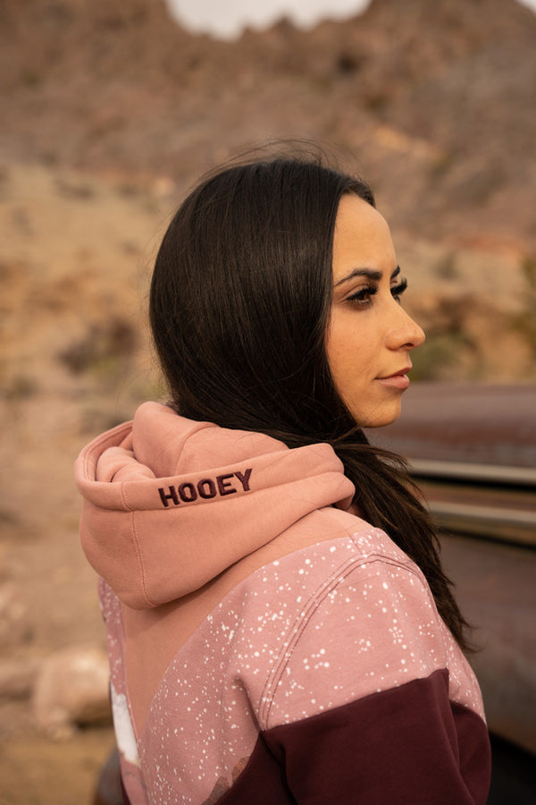 close up image of a model wearing the Berkley pink and maroon chevron pattern hoody with desert artwork