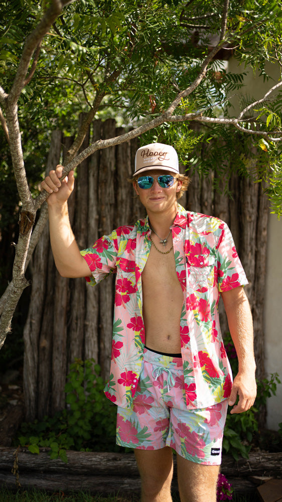 male model wearing tan hat with Hawaiian print board shorts and button down