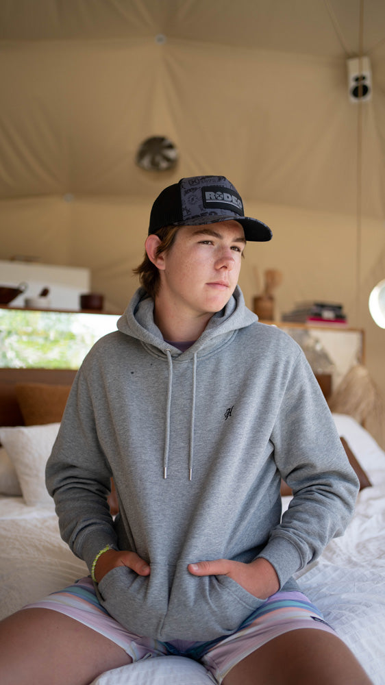 young male modeling pink and blue board shorts, heather grey hoody and black hooey hat 