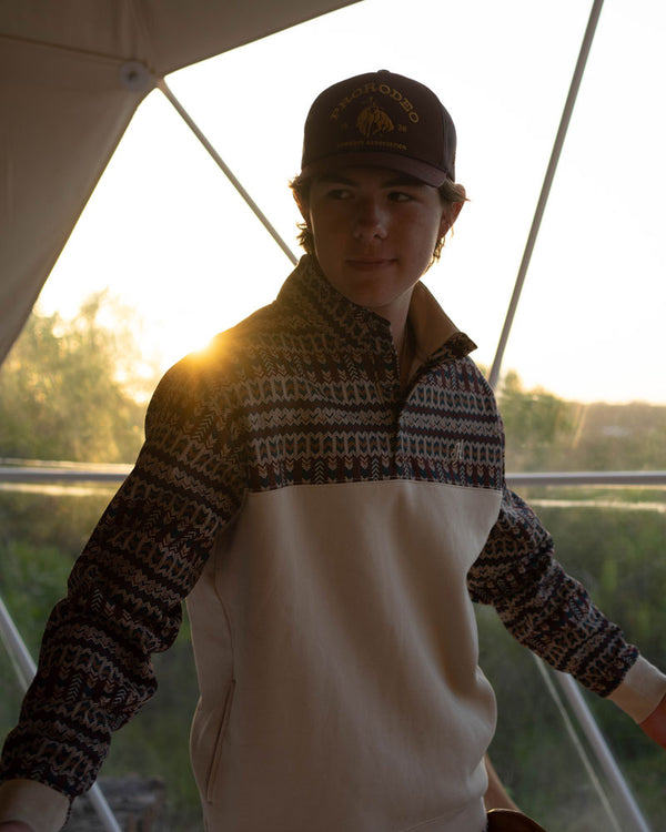 young male model posing on boat in outdoor setting wearing tan and brown Aztec pullover 
