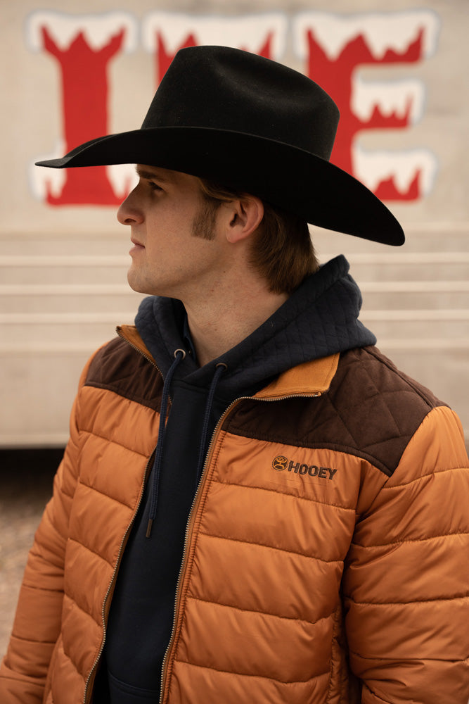 Close-up profile photo of male model for a black felt cowboy hat black hoodie and brown and tan puffer jacket
