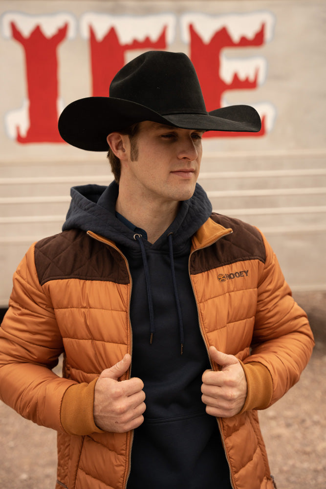 Male model wearing black hoodie orange and brown puffer jacket black felt cowboy hat