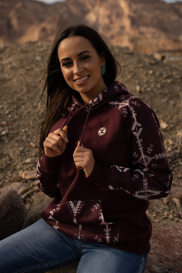 female model wearing the Summit maroon hoody with cream and blue aztec pattern on pocket and sleeves and hood with jeans in outdoor setting