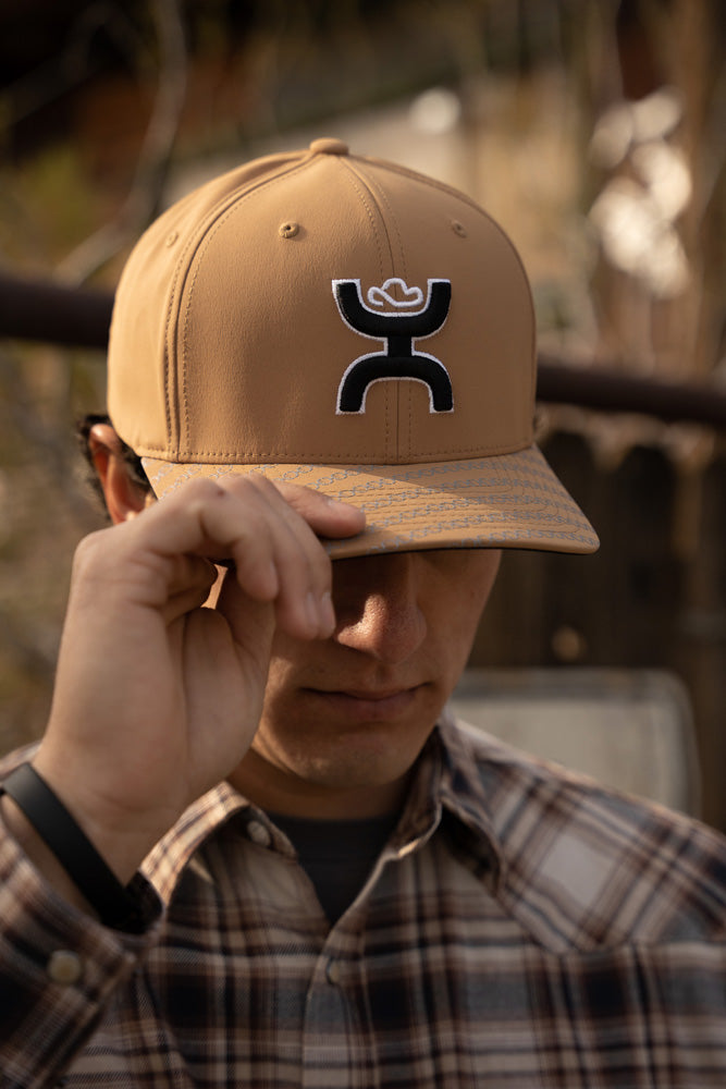 male model wearing tan hat with black and white logo and brown, black, white plaid shacket