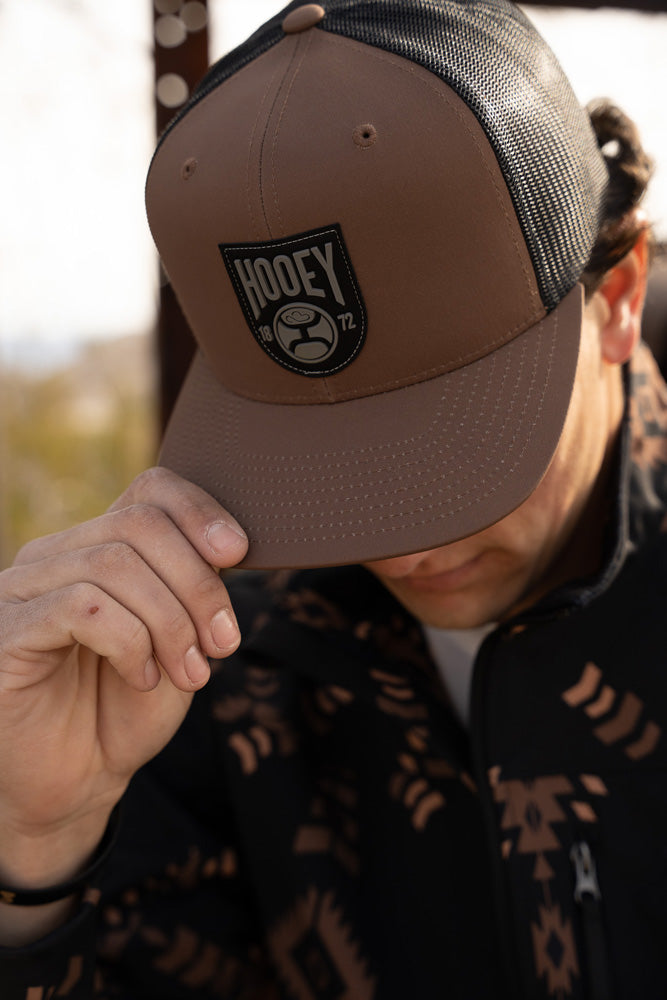 male model wearing brown and black hooey cap with black and brown aztec pattern tech jacket
