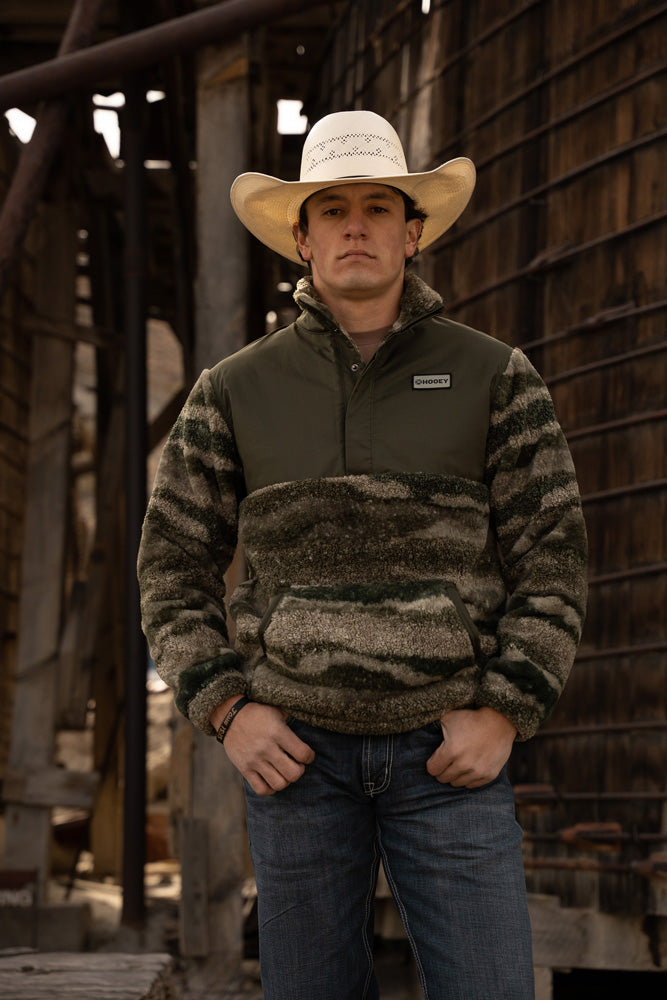male model wearing dark wash jeans, green camo pullover and straw cowboy hat