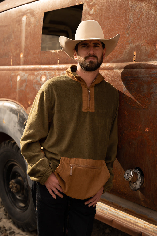 male model wearing olive and tan pullover, tan cowboy hat, and black jeans