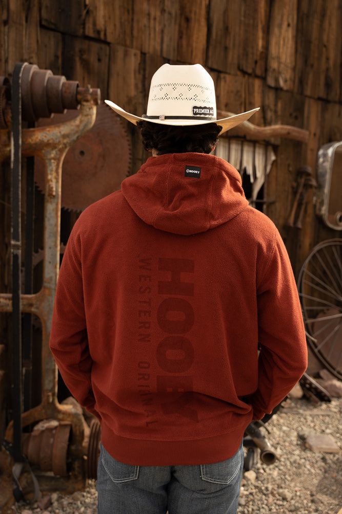back of the shadow red hoody with Hooey logo on back on male model wearing straw cowboy hat infront of rustic garage