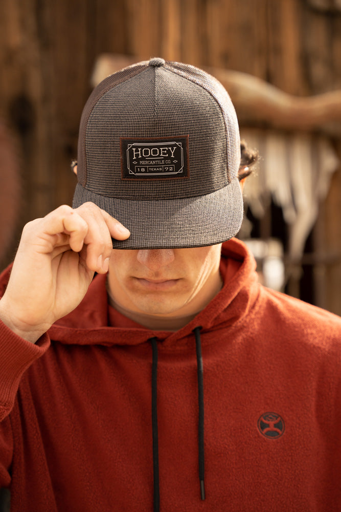 male model wearing grey hooey hat pulled over eyes with right hand and rust fleece hoody
