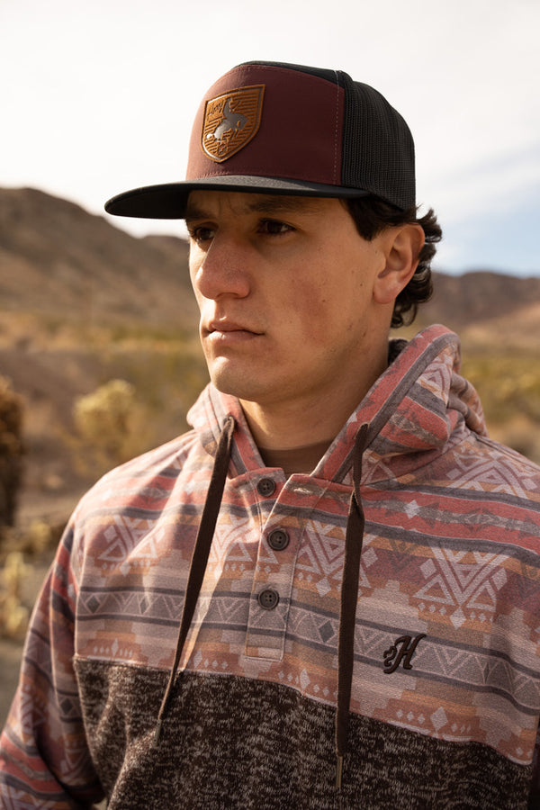 male model sporting the Jimmy heathered grey hoody with purple quilt pattern on sleeves, hood, and collar, roughy hat in mountainous setting