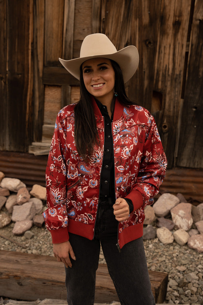 close up of female model posing in red, floral bomber jacket, cream cowboy hat, and dark pants.